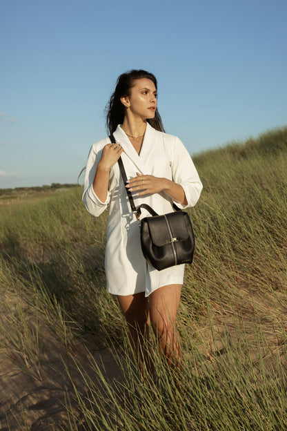 Sac à main bandoulière noir porté par une femme avec une robe blazer blanche_